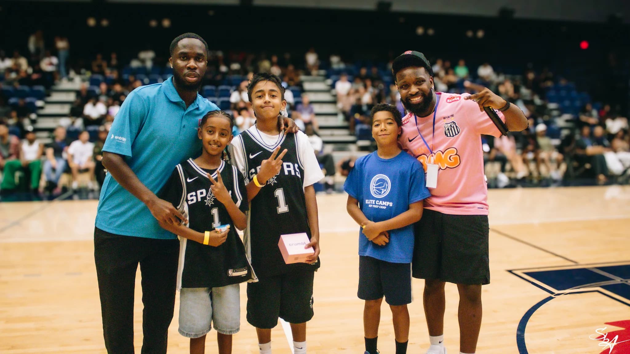 Three young attendees pose with two adult community members on the basketball court.